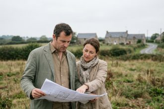 Couple examinant des plans de construction sur un terrain à bâtir en périphérie de Rennes